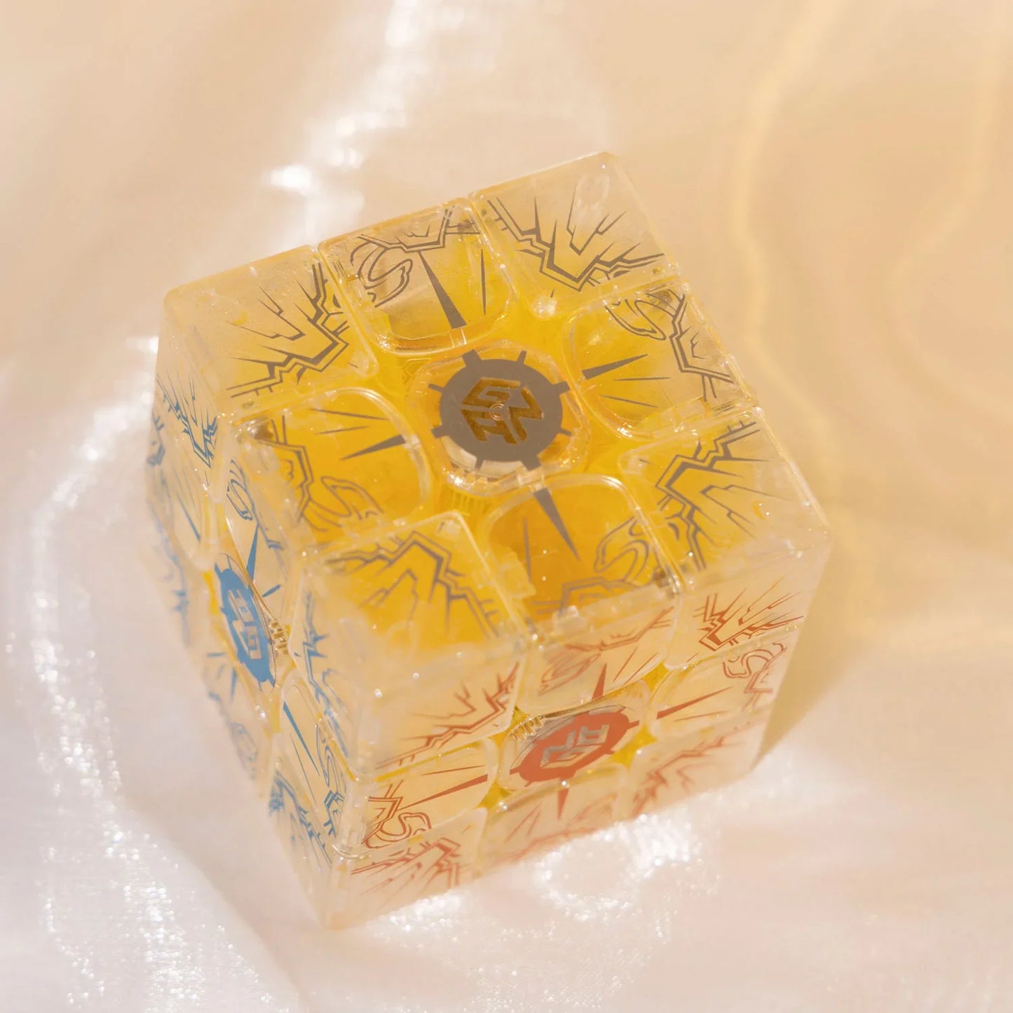 Transparent yellow 3x3 Rubik's Cube puzzle with lightning and gear designs on a soft beige surface