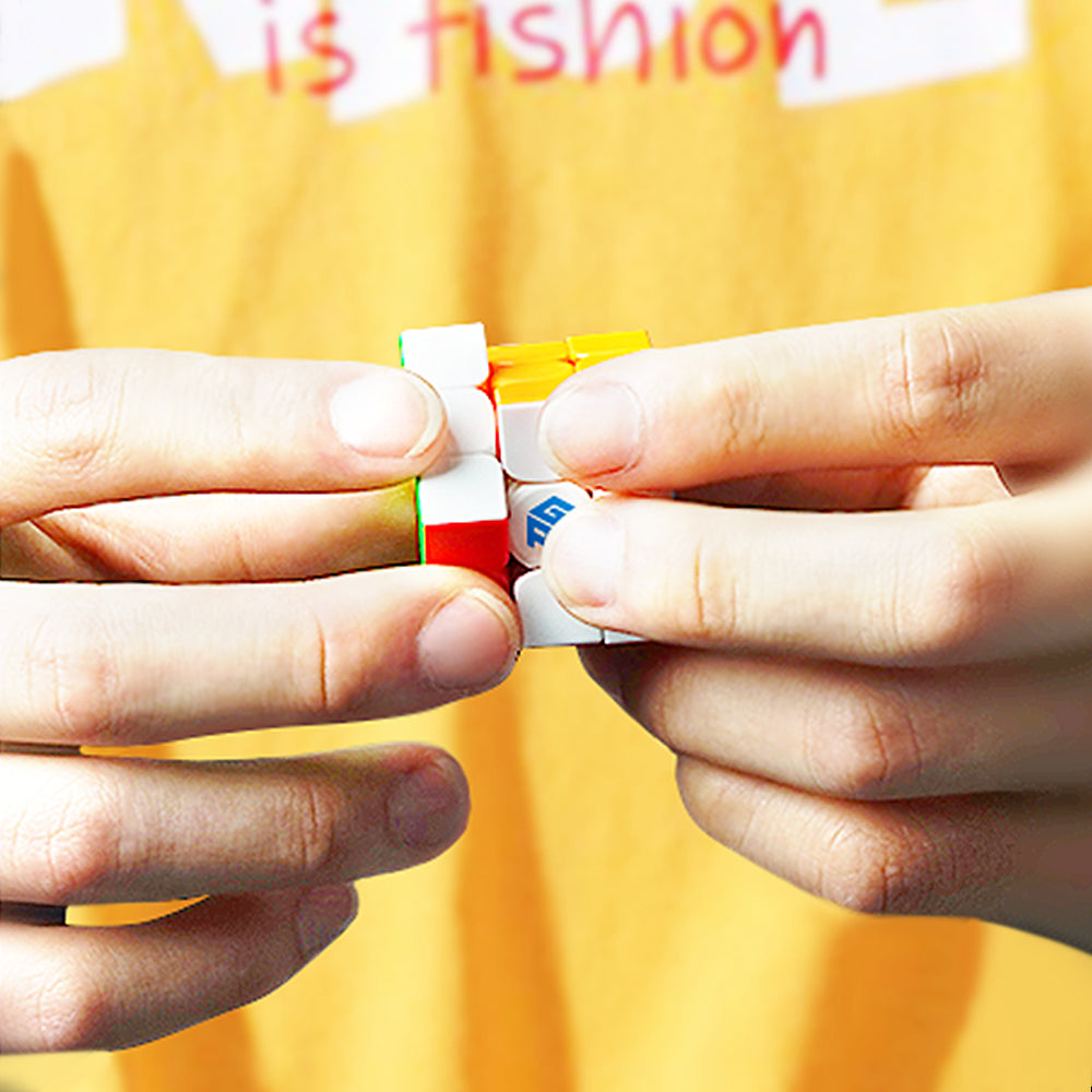 Close-up of hands solving a GAN Cube 3x3 Rubik's puzzle against a yellow shirt background
