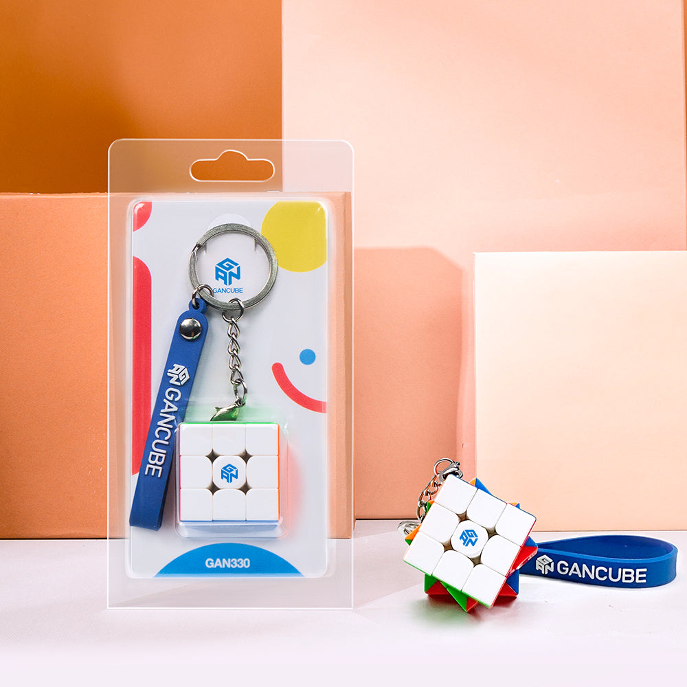 GAN330 mini Rubik's Cube keychain with blue GAN wristband on orange and peach background