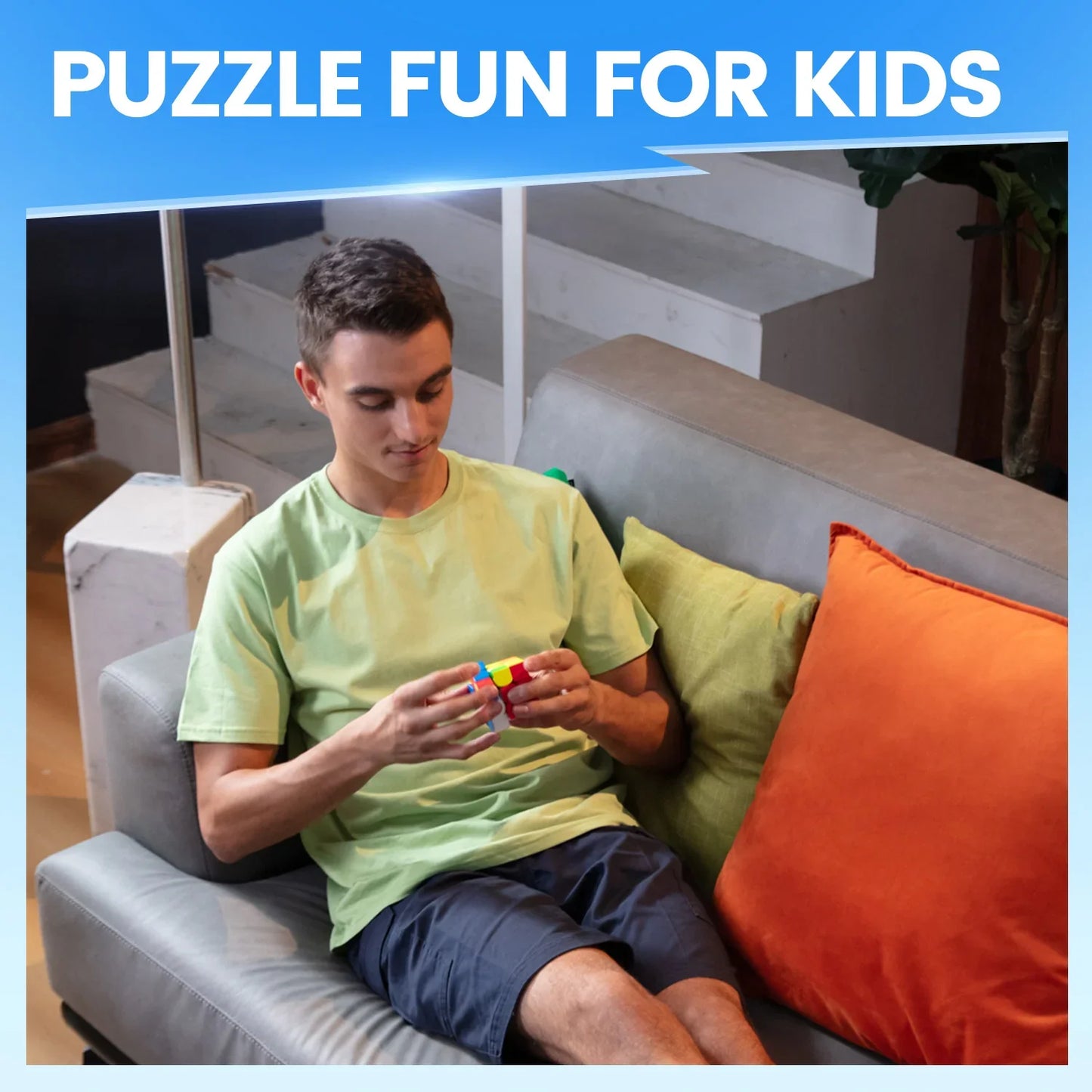 Young man sitting on gray couch solving a colorful Rubik's Cube puzzle with bright cushions