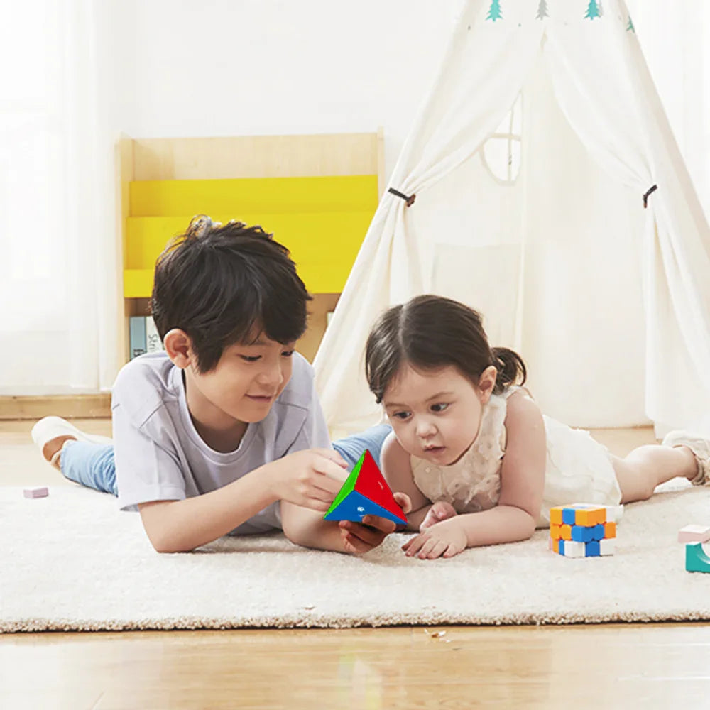 Two children playing indoors on a rug with a colorful GAN Pyraminx puzzle and a Rubik's cube toy