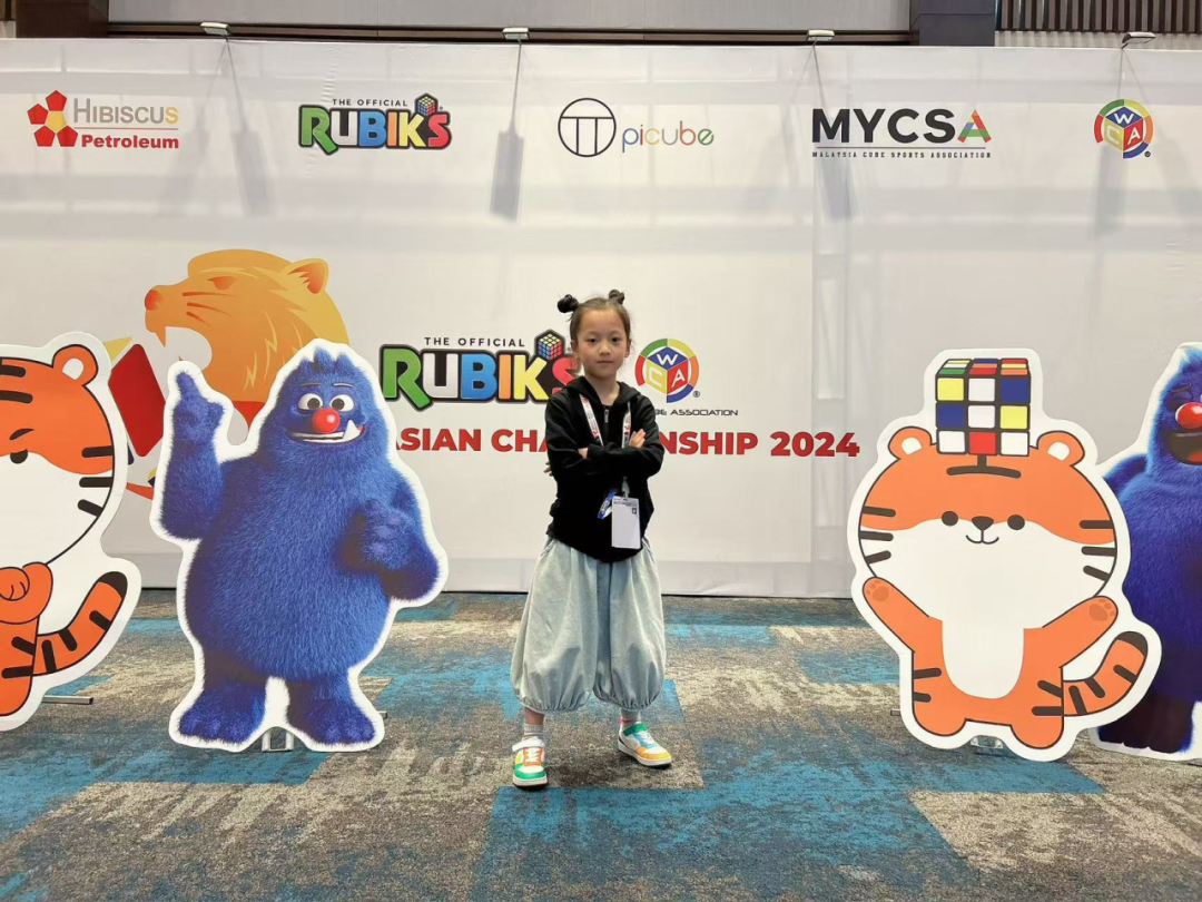 Young girl posing at the Official Rubik's Asian Championship 2024 with colorful cartoon mascots