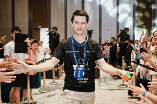 Young man holding a Rubik's Cube high fives fans at a cubing event with spectators and cameras