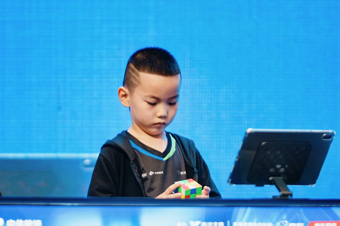 Young boy solving a speed cube at a competition with a digital timer on the table