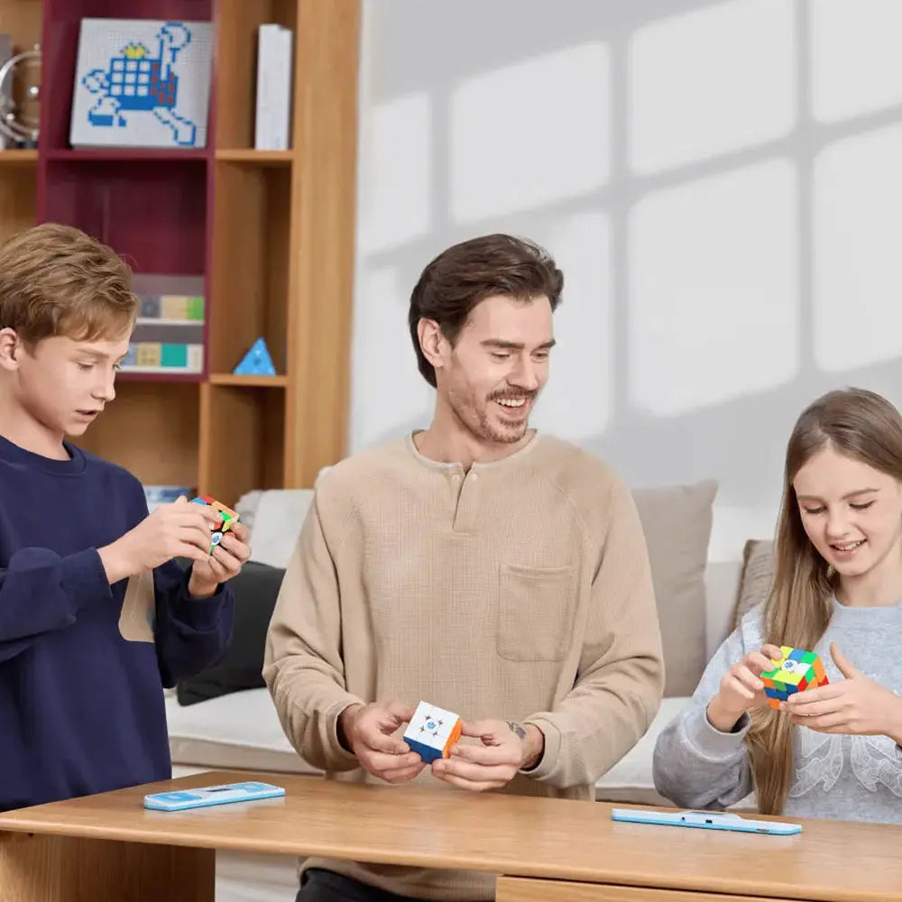 Man and two children solving colorful GANCUBE speed cubes at wooden table in bright room