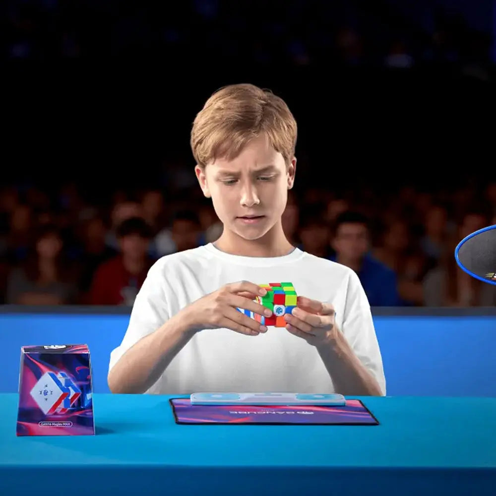 Young boy focused on solving a colorful GAN speedcube at a blue table with audience blurred in background