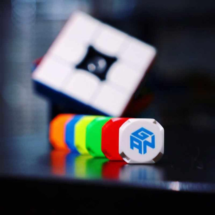 GANCUBE white center cap with blue logo, colorful puzzle cube parts in a row, blurred cube background